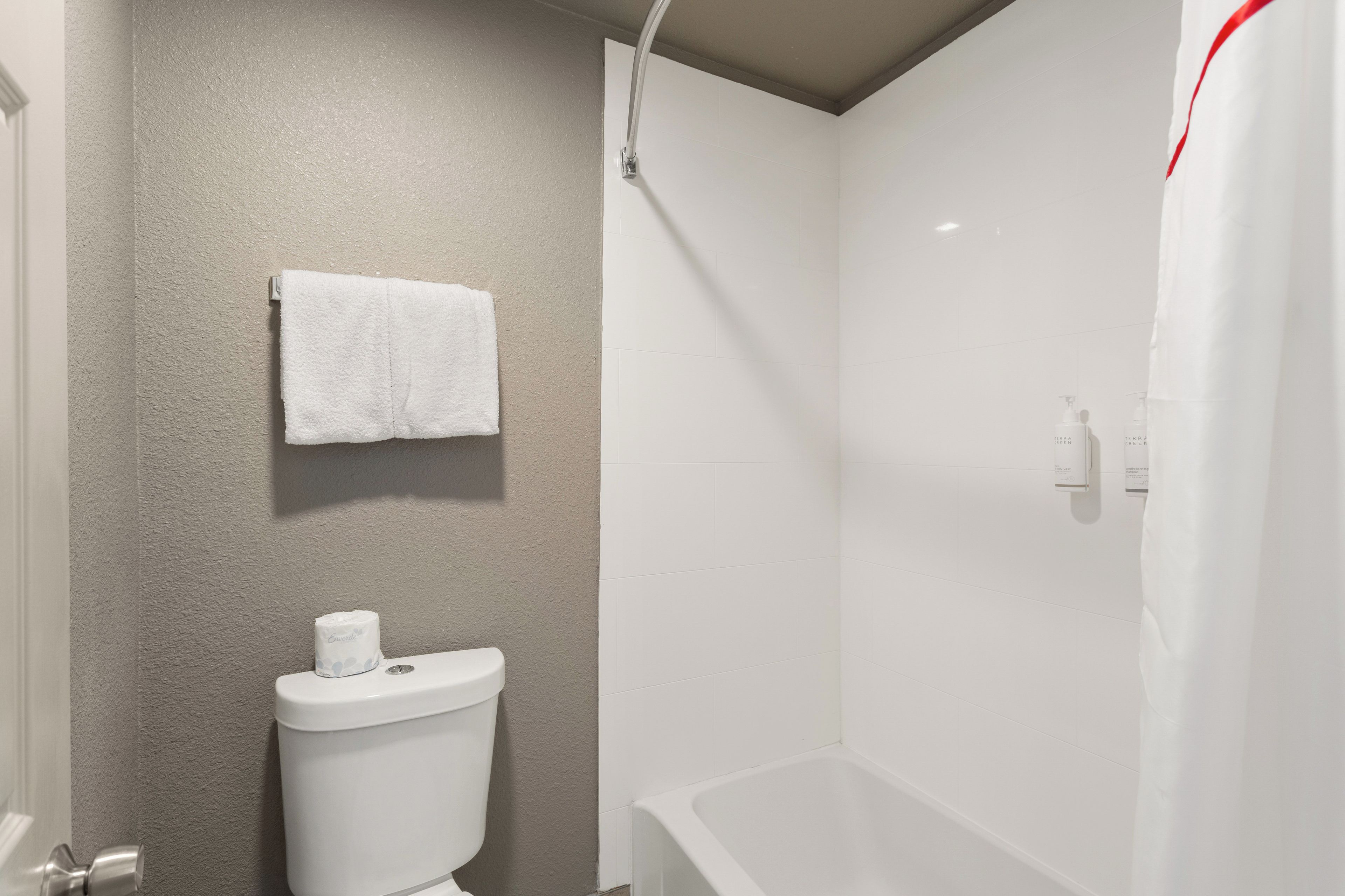 Un baño con inodoro, una toalla colgada en la pared y zona de ducha.