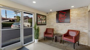 Une réception avec l’enseigne d’un Red Roof Inn, deux fauteuils en cuir, une plante en pot et une vue sur le parking.