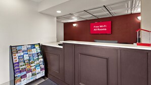 Un espace d’accueil avec un mur rouge, un comptoir blanc et un panneau indiquant : « Wi-Fi gratuit dans toutes les chambres ».