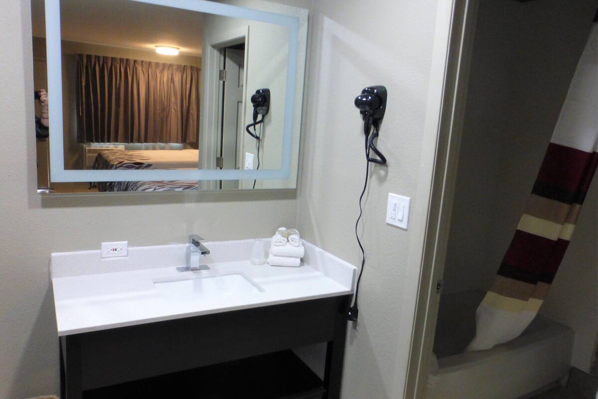 A hotel bathroom with a white sink, a mirror, and a hairdryer mounted on the wall.