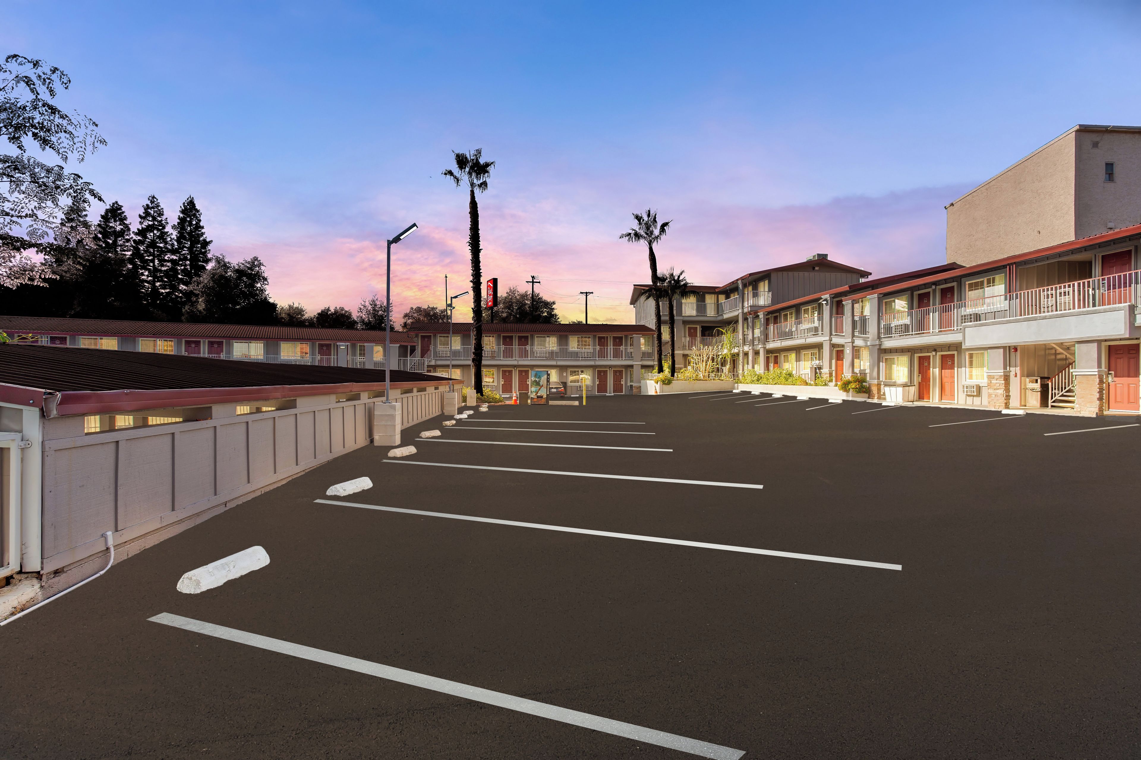 A motel with a row of rooms, a parking lot, and a building with a balcony.