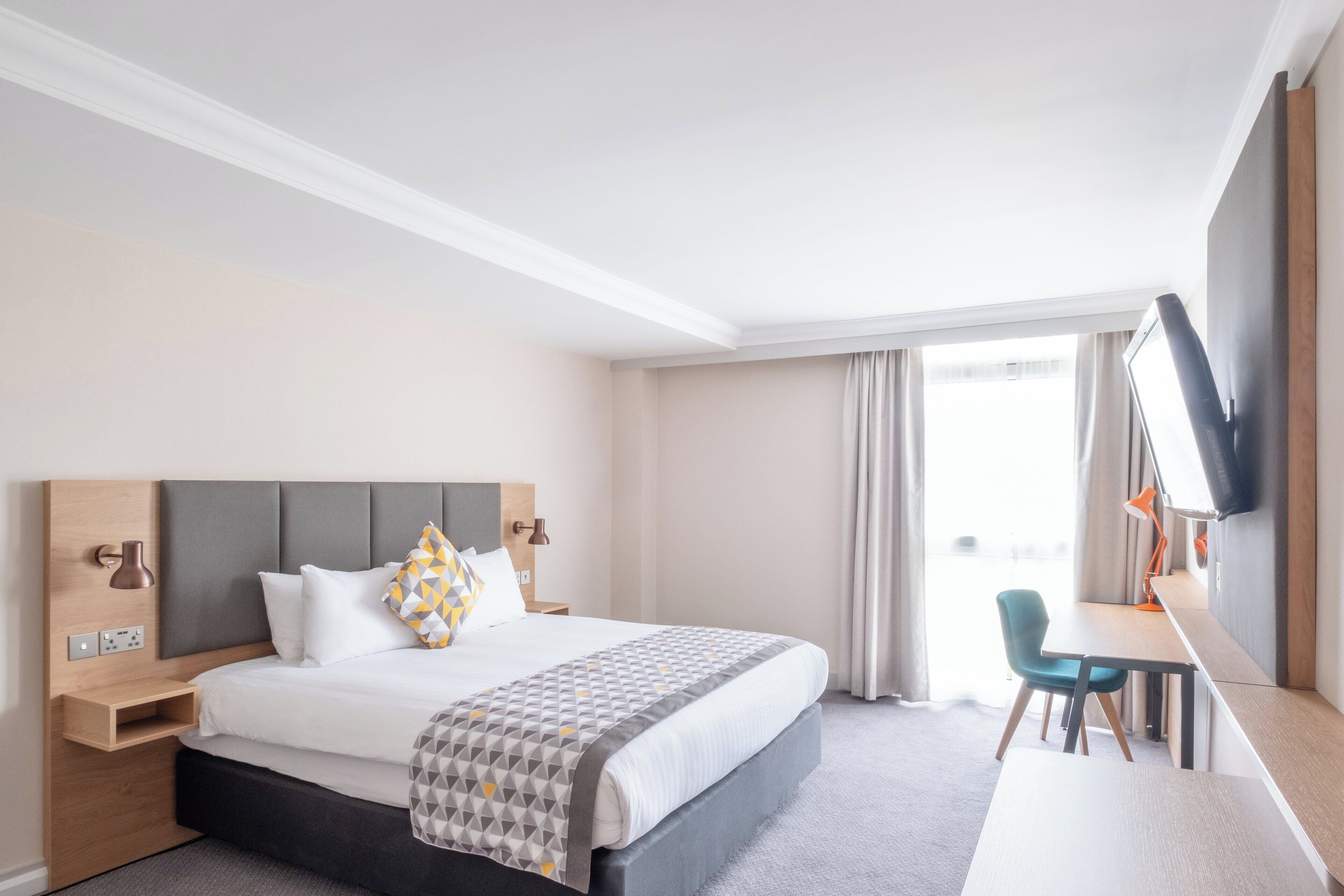 A hotel room with a bed, bedside tables, a desk, and a TV.