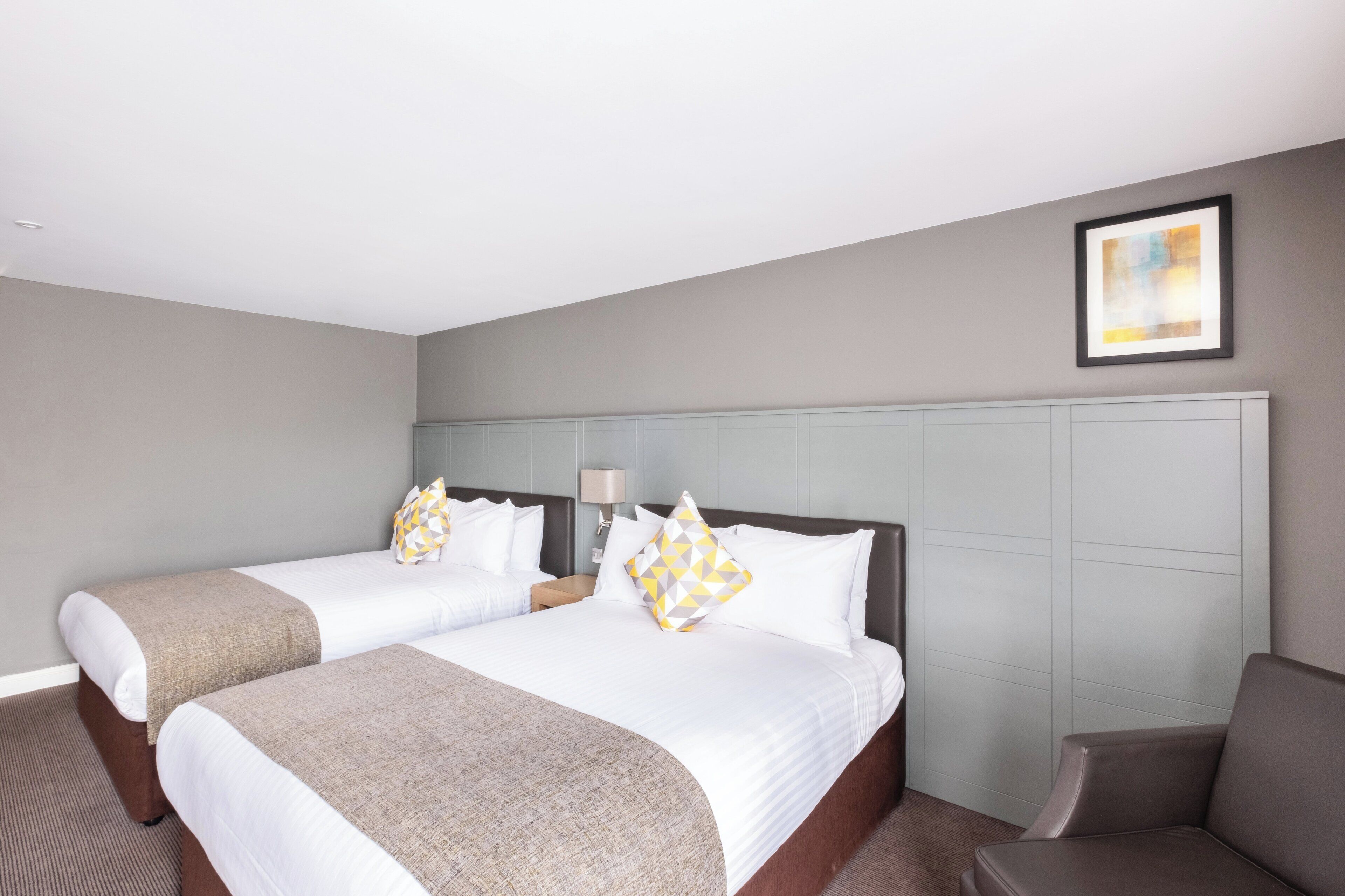 A hotel room with two beds, a nightstand, a chair, and a painting on the wall.