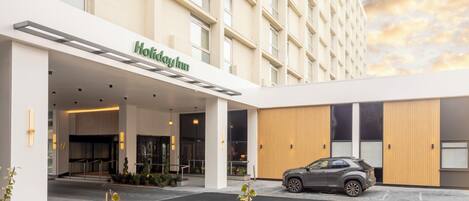 A Holiday Inn hotel entrance with a covered driveway, a parked car, and a modern building facade.