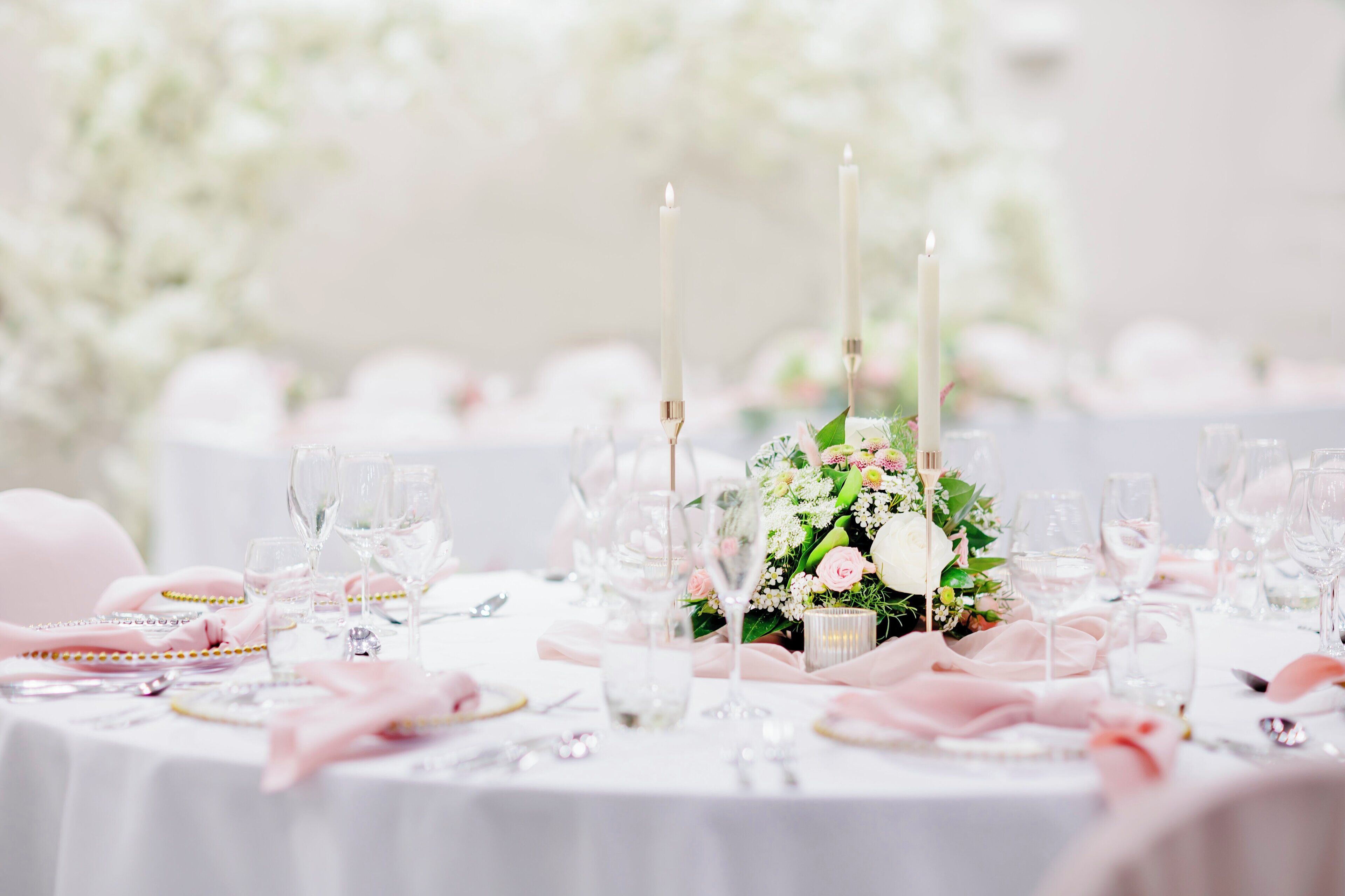 Une table dressée avec des nappes blanches, des serviettes roses et de la verrerie transparente.
