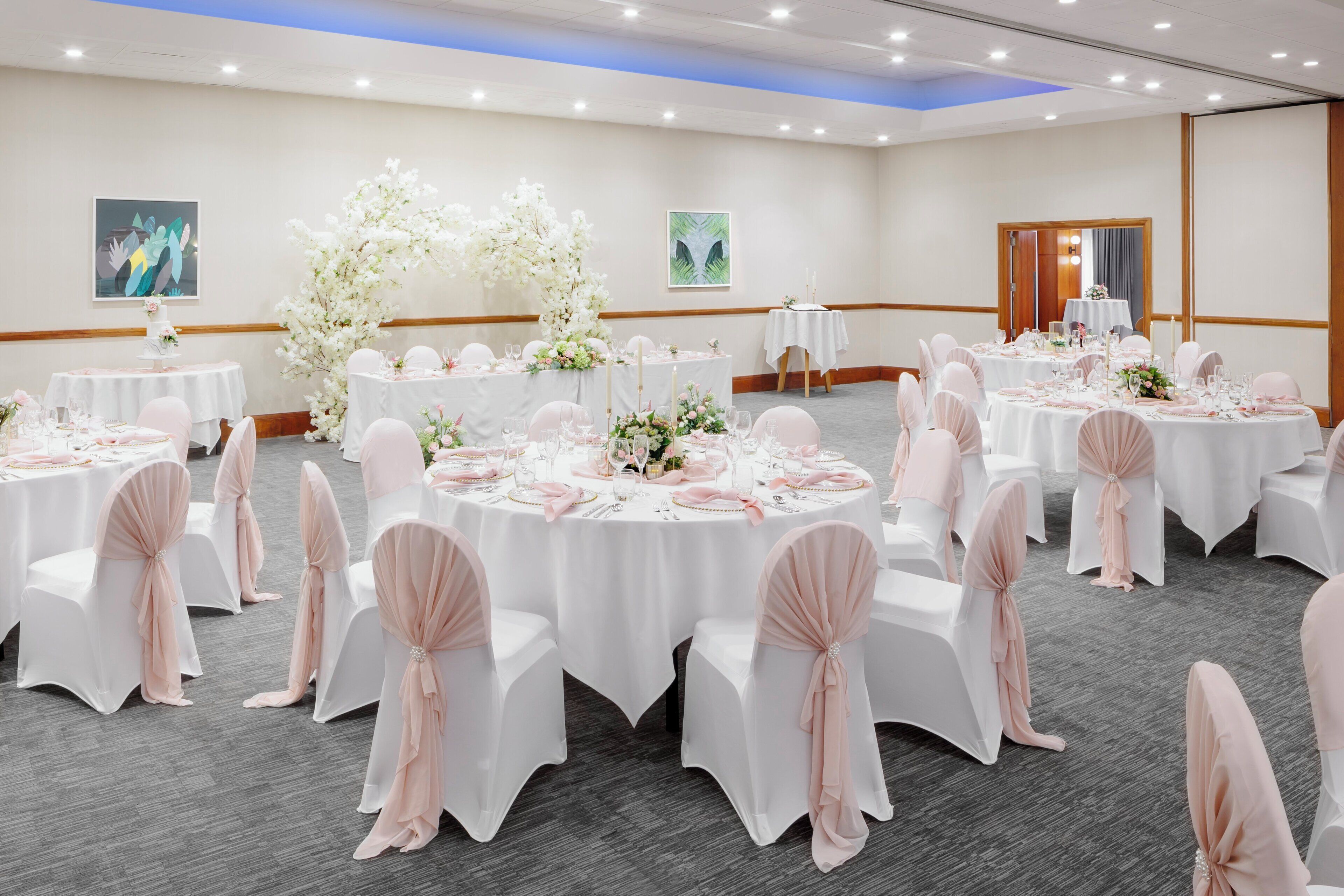 A banquet hall with round tables, white tablecloths, and chairs with pink sashes.