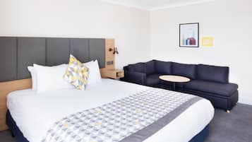 Una camera d'albergo con un letto grande, un divano, un tavolino rotondo e una lampada a parete.
