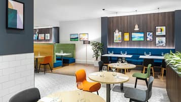 A modern restaurant with round tables, orange and gray chairs, and a blue booth seating area.