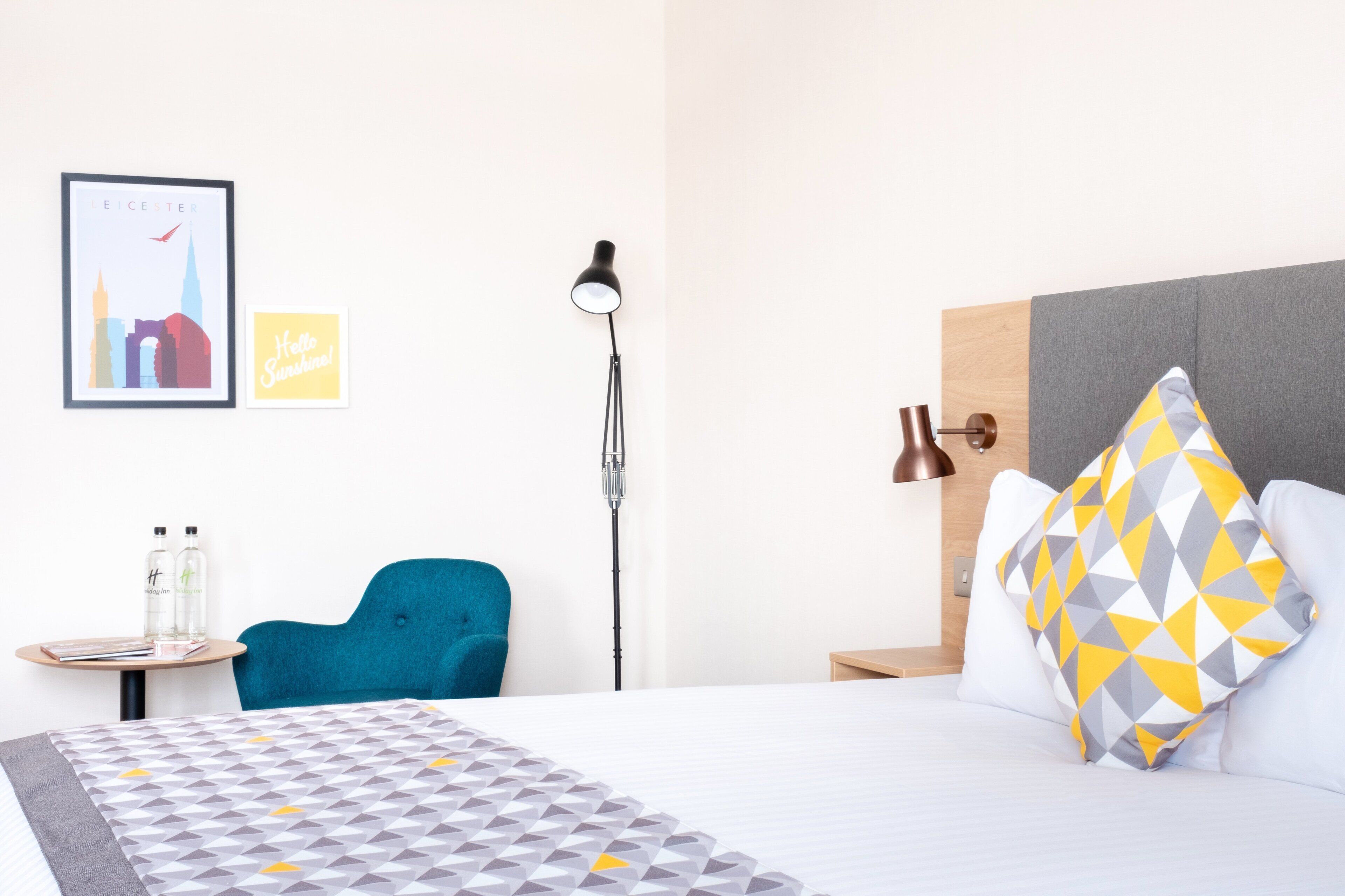 A hotel room with a bed, a desk, a chair, a lamp, and a framed picture on the wall.