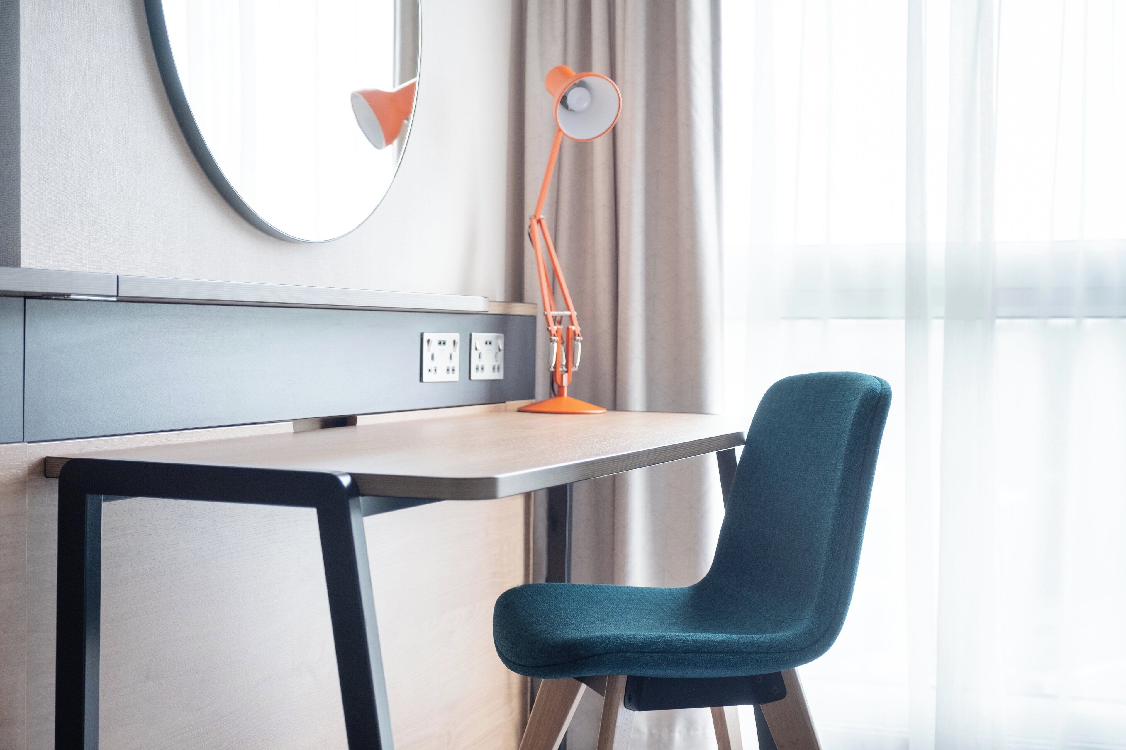 A modern office desk with a chair, a round mirror, and an adjustable desk lamp.
