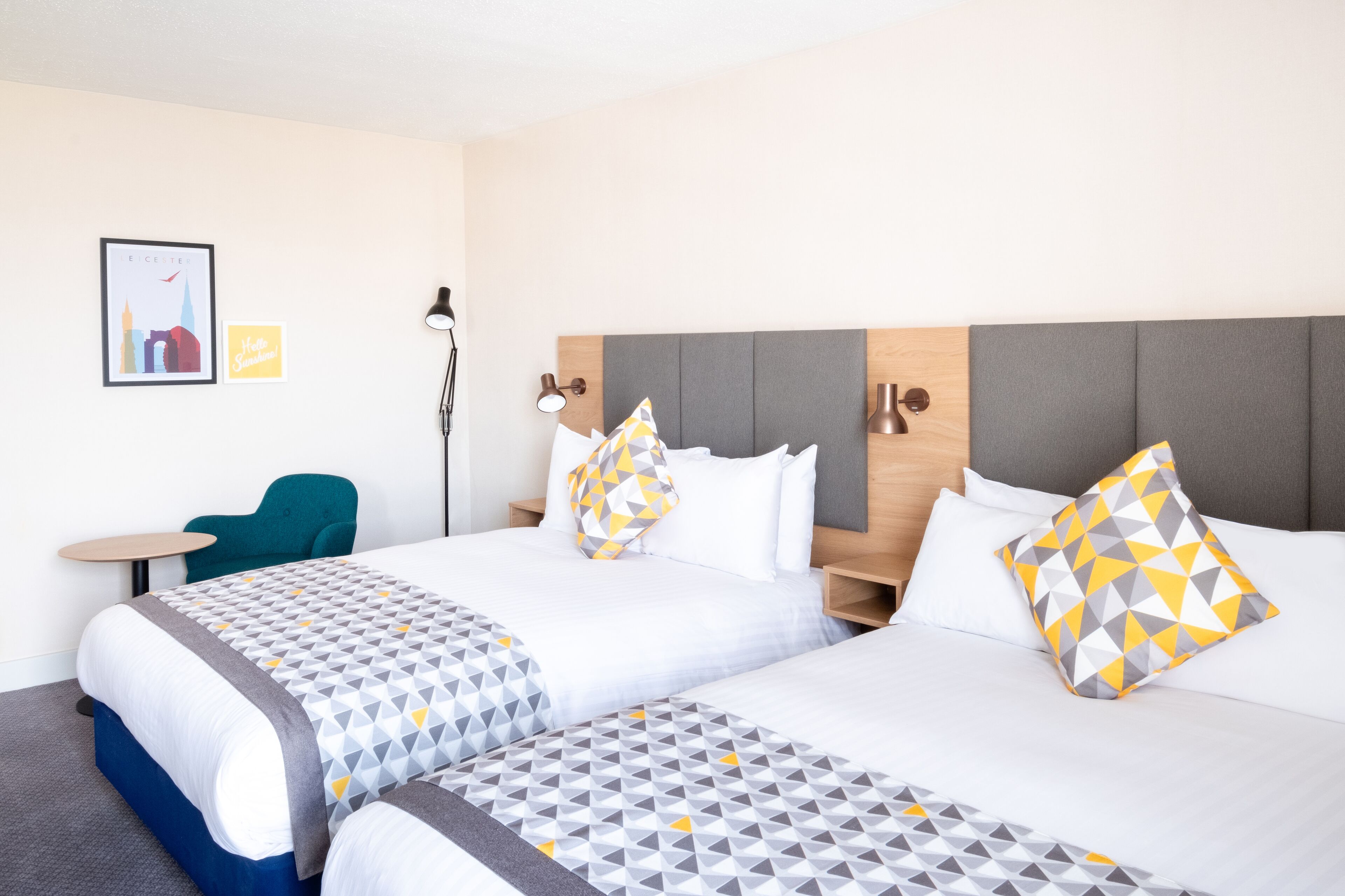 A hotel room with two beds, a desk, a chair, and a lamp.