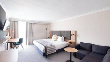 A hotel room with a bed, a desk, a chair, a sofa, and a TV.