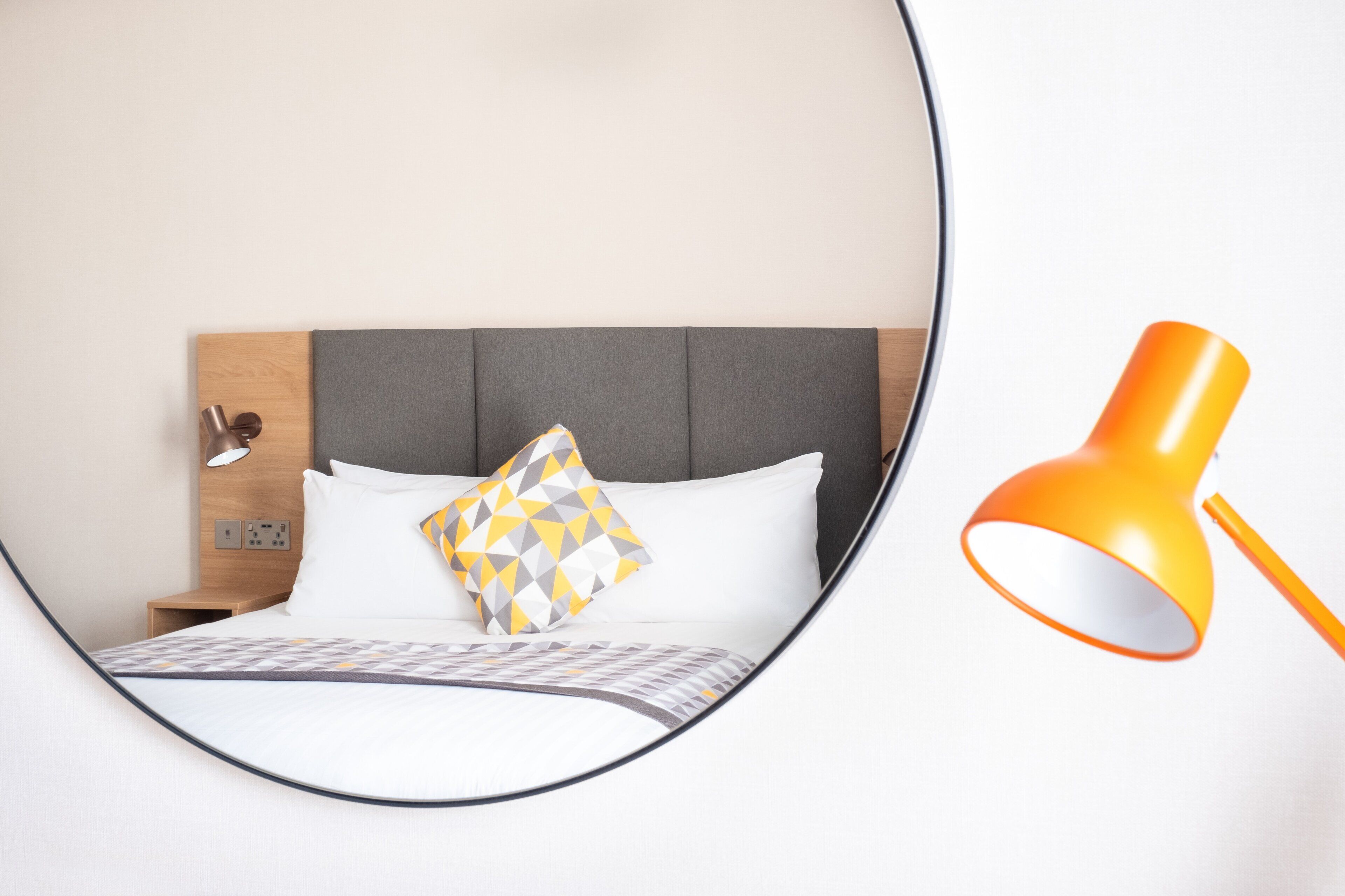 Una cama bien hecha con un cojín de estampado geométrico, una mesita de noche con lámpara y un cabecero moderno.