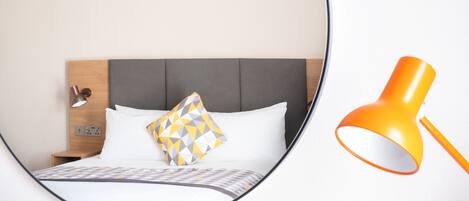 Uma cama bem arrumada com almofada de padrão geométrico, uma mesa de cabeceira com abajur e uma cabeceira moderna.