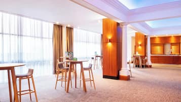 A hotel lobby with high ceilings, large windows, and a central seating area with tables and chairs.
