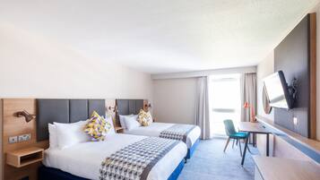 Una habitación de hotel con dos camas, un escritorio, una silla, un televisor y una ventana con cortinas.