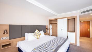 Een hotelkamer met een bed, nachtkastje, garderobe en een badkamer door een geopende deur.