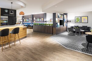A modern hotel lobby with a bar area, seating, and a reception desk.