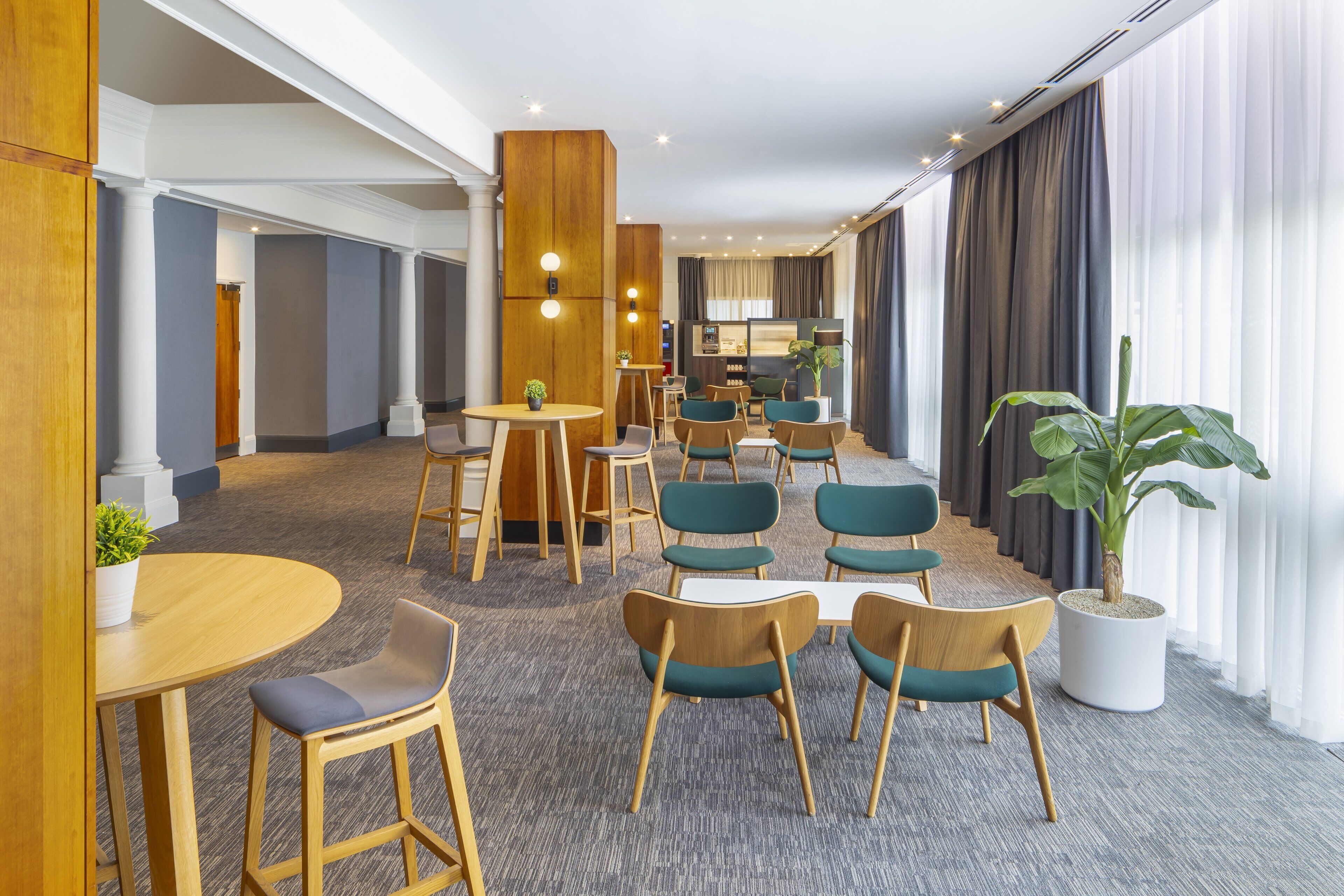 Um lobby de hotel com design moderno, apresentando uma combinação de mobiliário de madeira e estofado, uma área de estar central e uma grande planta em vaso.