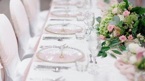 A table set with pink plates, clear glasses, and silverware, accompanied by a floral centerpiece. - Holiday Inn Leicester by IHG (Leicester)