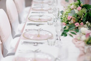 A table set with pink plates, clear glasses, and silverware, accompanied by a floral centerpiece.