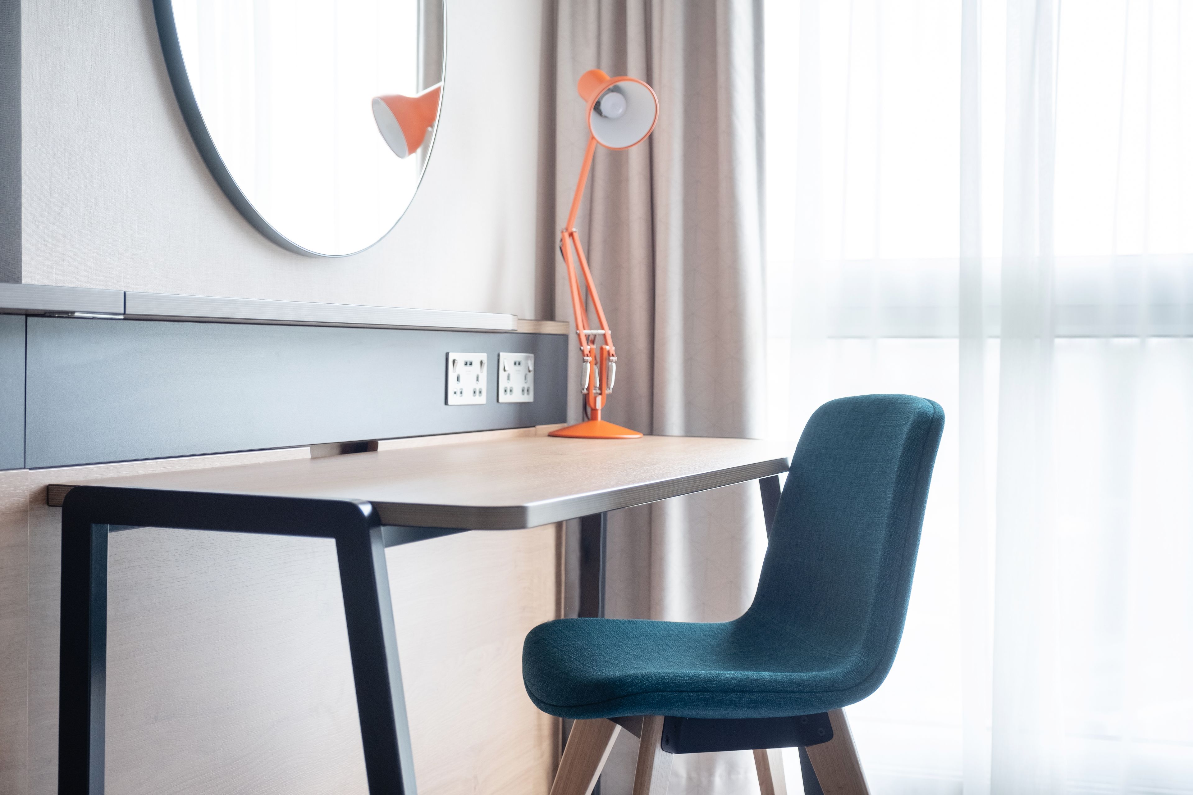 A modern room with a desk, chair, lamp, and a large mirror on the wall.
