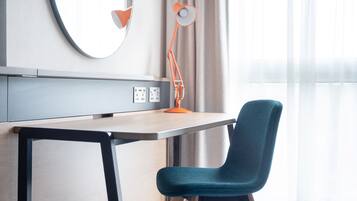 A modern room with a desk, chair, lamp, and a large mirror on the wall.