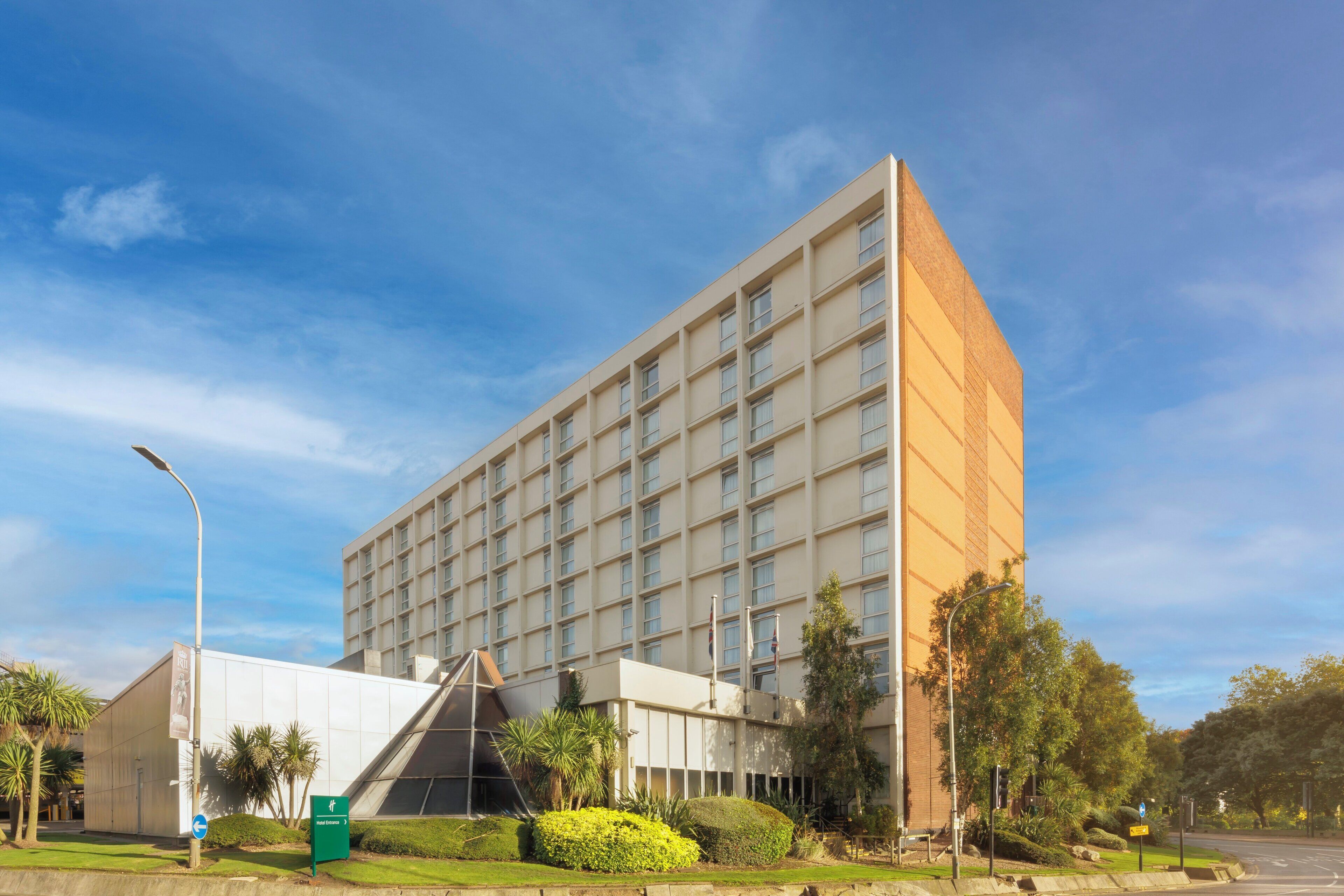 A modern building with a grid of windows, a green sign, and well-maintained landscaping.