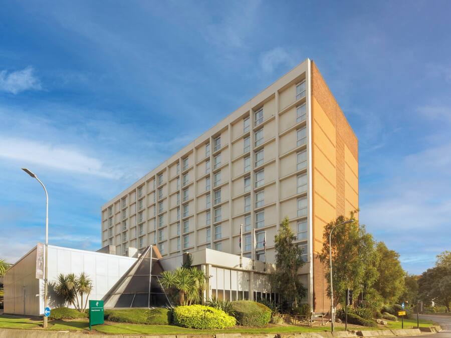 A modern building with a grid of windows, a green sign, and well-maintained landscaping.
