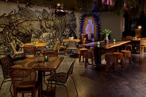 A restaurant interior with wooden tables and chairs, a mural on the wall, and hanging plants. - Hotel Rendale Washington DC (Washington)