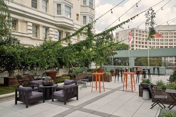 Un patio al aire libre con asientos, macetas y vista a un edificio al fondo.