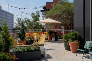 An outdoor seating area with chairs and tables, potted plants, and a large umbrella.