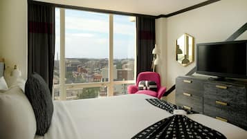 Een hotelkamer met een groot raam, een bed, een televisie, een dressoir en een stoel.