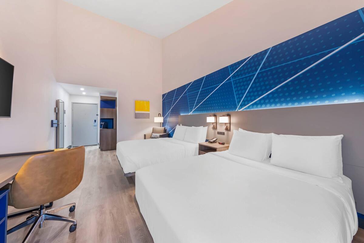 Hotellihuone, jossa on kaksi sänkyä, työpöytä, tuoli ja moderni seinäkoriste.