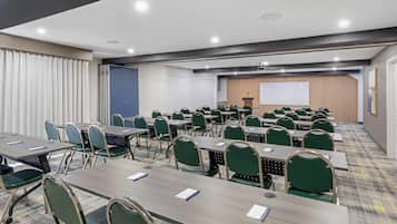 Une salle de conférence équipée de plusieurs tables et chaises, d’un écran de projection et d’un pupitre.