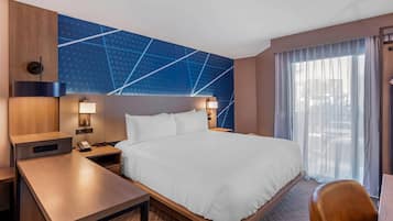 Une chambre d’hôtel comprenant un lit, des tables de chevet, un bureau, une horloge murale et une grande fenêtre avec des rideaux.