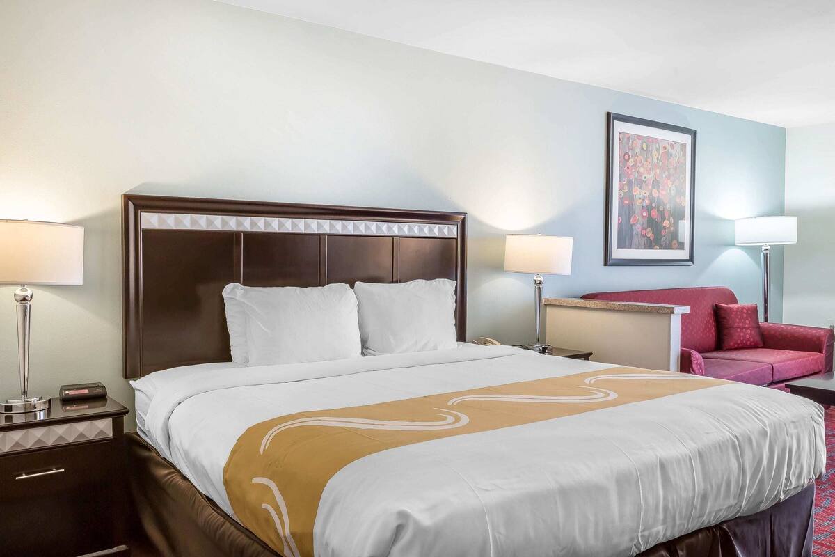 Une chambre d’hôtel avec un grand lit, des lampes de chevet, un canapé rouge et une œuvre d’art encadrée au mur.