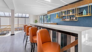 A modern bar area with a long counter, orange bar stools, and a blue accent wall. - Comfort Inn & Suites Irvine Spectrum (Lake Forest)
