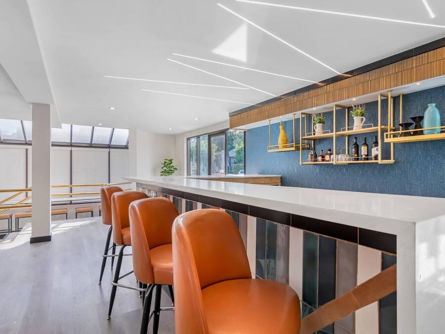 Un área de bar moderna con una barra alargada, taburetes naranjas y una pared azul de acento.