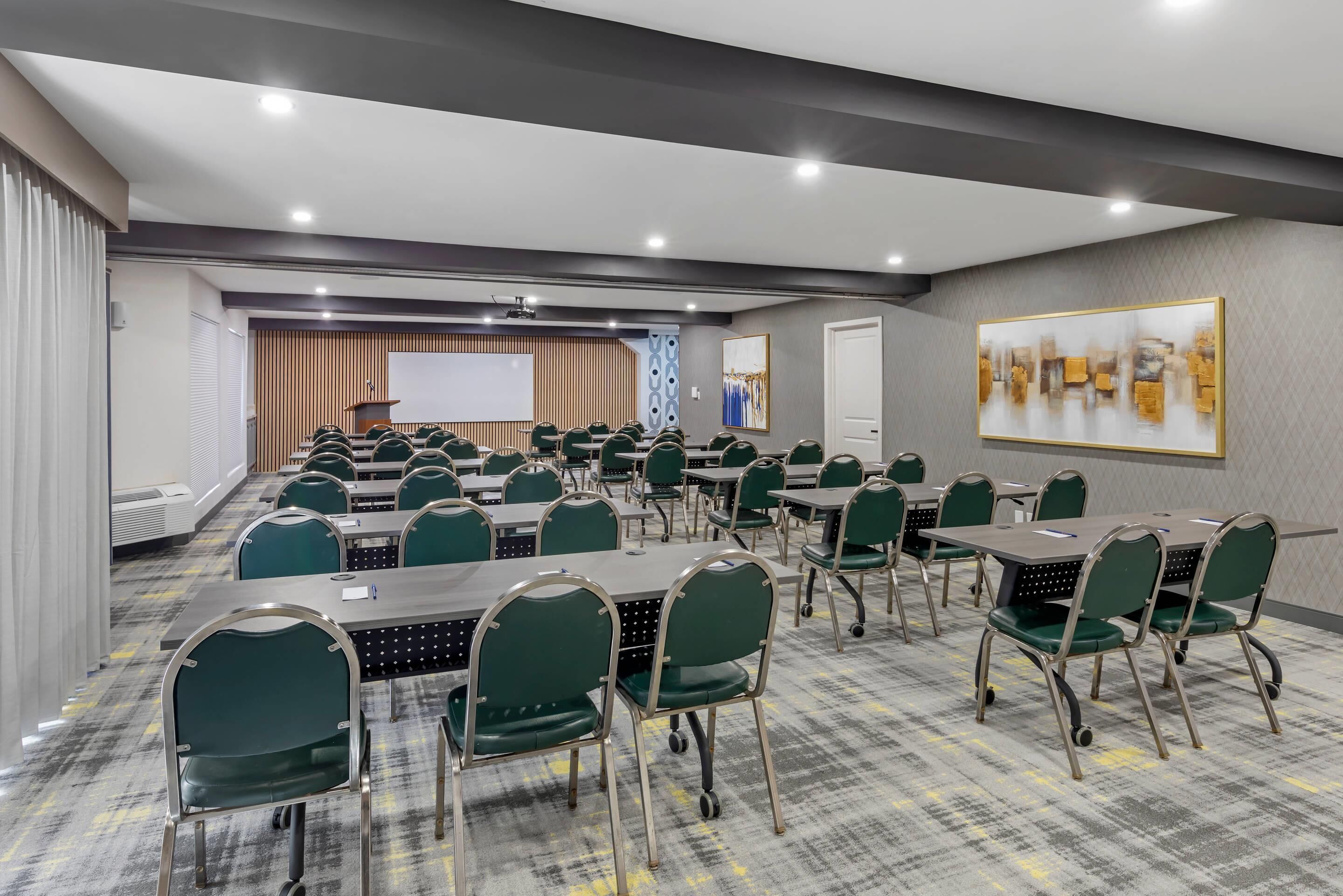 Una sala de conferencias con varias mesas y sillas, una pantalla de proyector y un espacio para presentaciones.