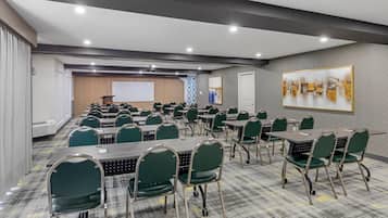 A conference room with multiple tables and chairs, a projector screen, and a presentation area.