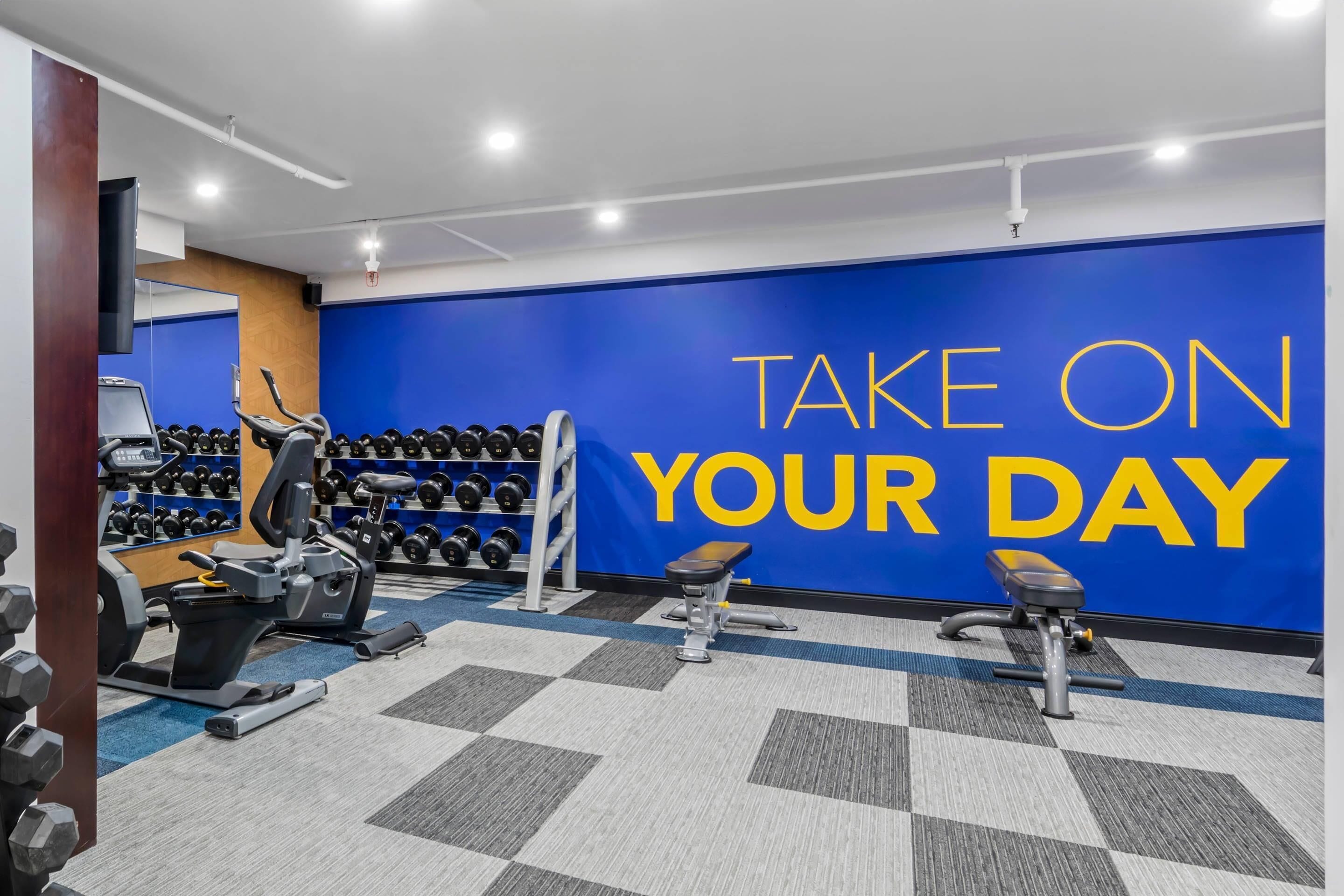 A gym with exercise equipment, a wall with motivational text, and a mirror.