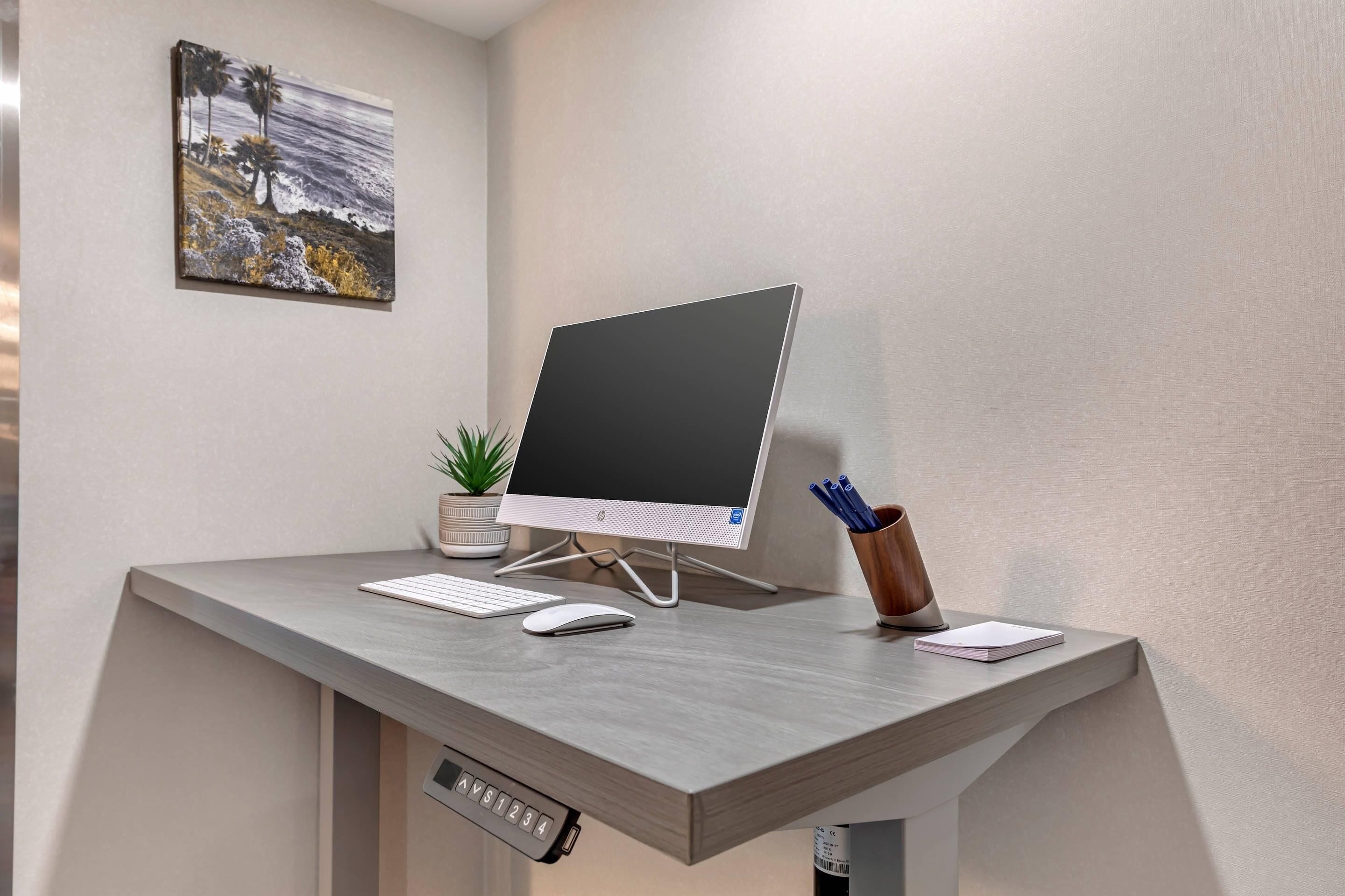A modern desk with a desktop computer, keyboard, mouse, and a small potted plant.