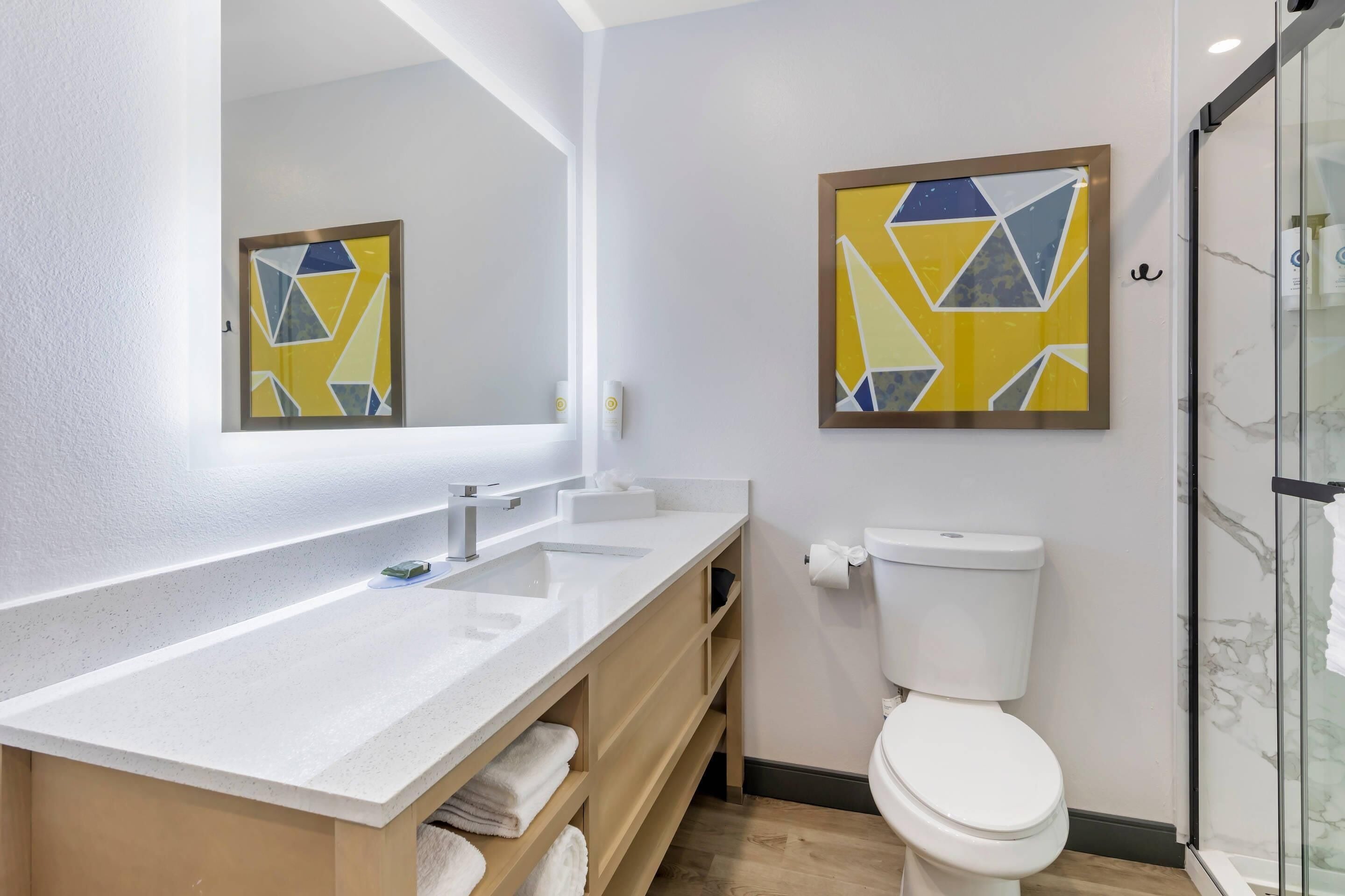 A modern bathroom with a white sink, mirror, and toilet. There are two abstract paintings on the walls.
