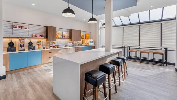 A modern kitchen with a central island, bar stools, and a view of the city through large windows. - Comfort Inn & Suites Irvine Spectrum (Lake Forest)