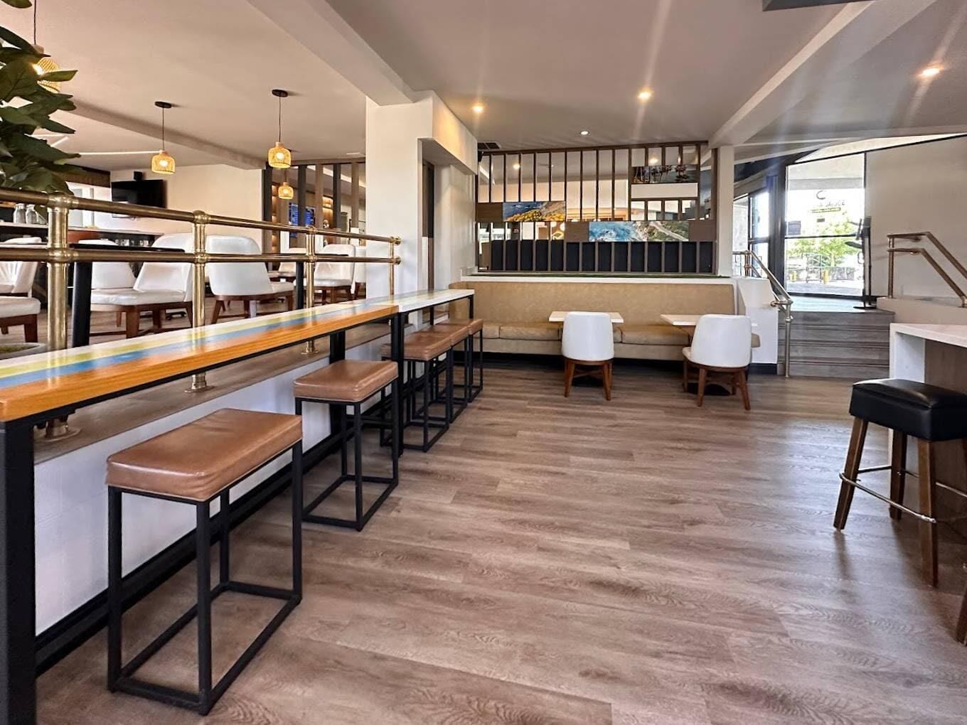 Uma área de bar moderna com banquetas de madeira, cadeiras brancas e um balcão longo.