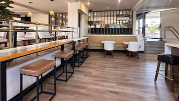 A modern bar area with wooden bar stools, white chairs, and a long counter.