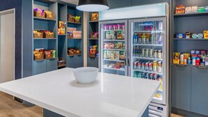 A modern kitchen with a white countertop, a bowl, and a refrigerator stocked with snacks and beverages. - Comfort Inn & Suites Irvine Spectrum (Lake Forest)