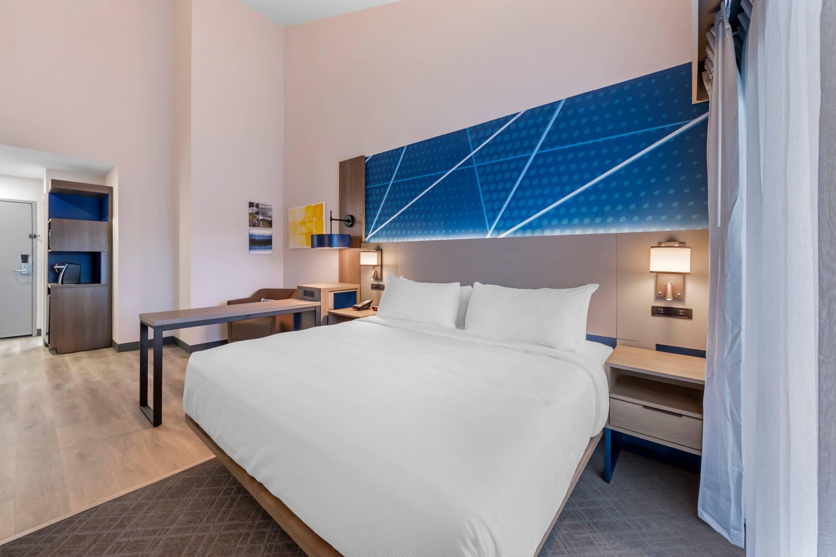 A hotel room with a large bed, bedside tables, a desk, a wardrobe, and a bathroom visible through an open door.