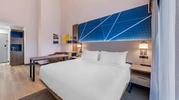 A hotel room with a large bed, bedside tables, a desk, a wardrobe, and a bathroom visible through an open door.